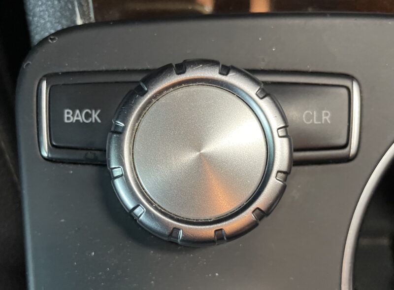 Center control wheel and buttons for a 2014 Mercedes Benz GLK - Mercedes calls this the "Command" wheel, after their name for this era of infotainment system. To the left of the silver wheel is a back button; to the right is a "clr" button.